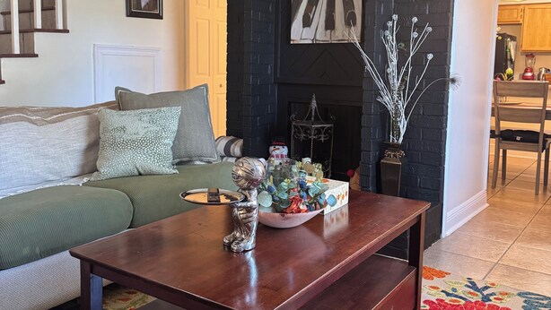 A living room with a dark fireplace, a green sofa, a wooden coffee table, and a colorful rug.