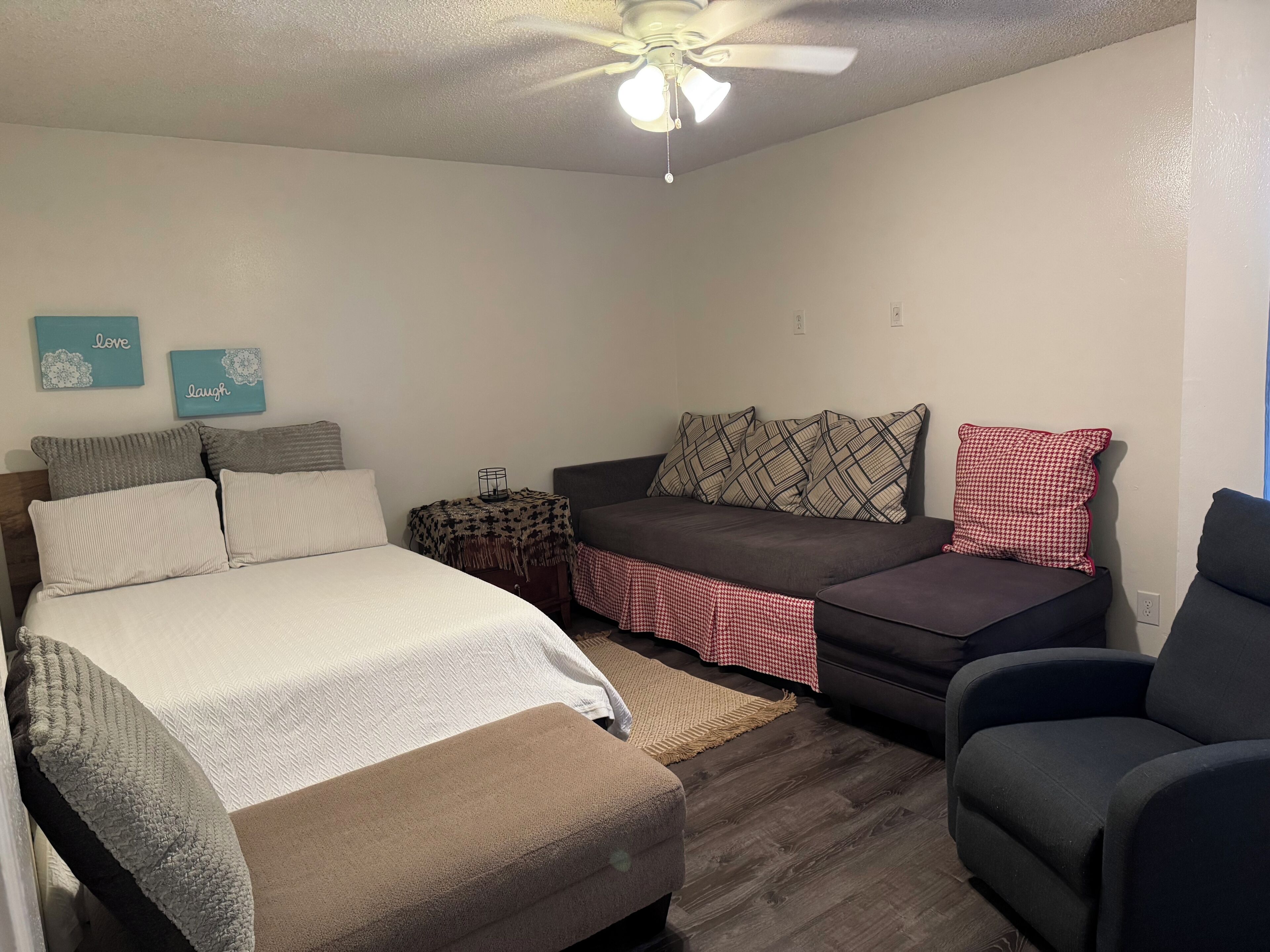 A bedroom with a bed, a sofa, a chair, and a ceiling fan.