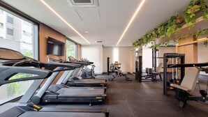 Ett gym med löpband, styrketräningsmaskiner och en växt som hänger på väggen.