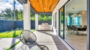 A modern patio with a wooden ceiling, a glass door leading to a dining area, and a kitchen with a built-in oven. - Fabulous 5-bedroom house in Dallas (Dallas)