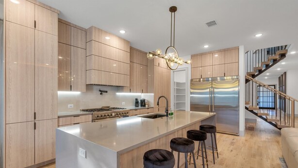 A modern kitchen with wooden cabinets, a central island with stools, a stainless steel refrigerator, and a staircase leading to a loft area. - Fabulous 5-bedroom house in Dallas (Dallas)