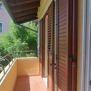 Ein Balkon mit Fliesenboden, einem Metallgeländer und einer Holztür mit Griff.
