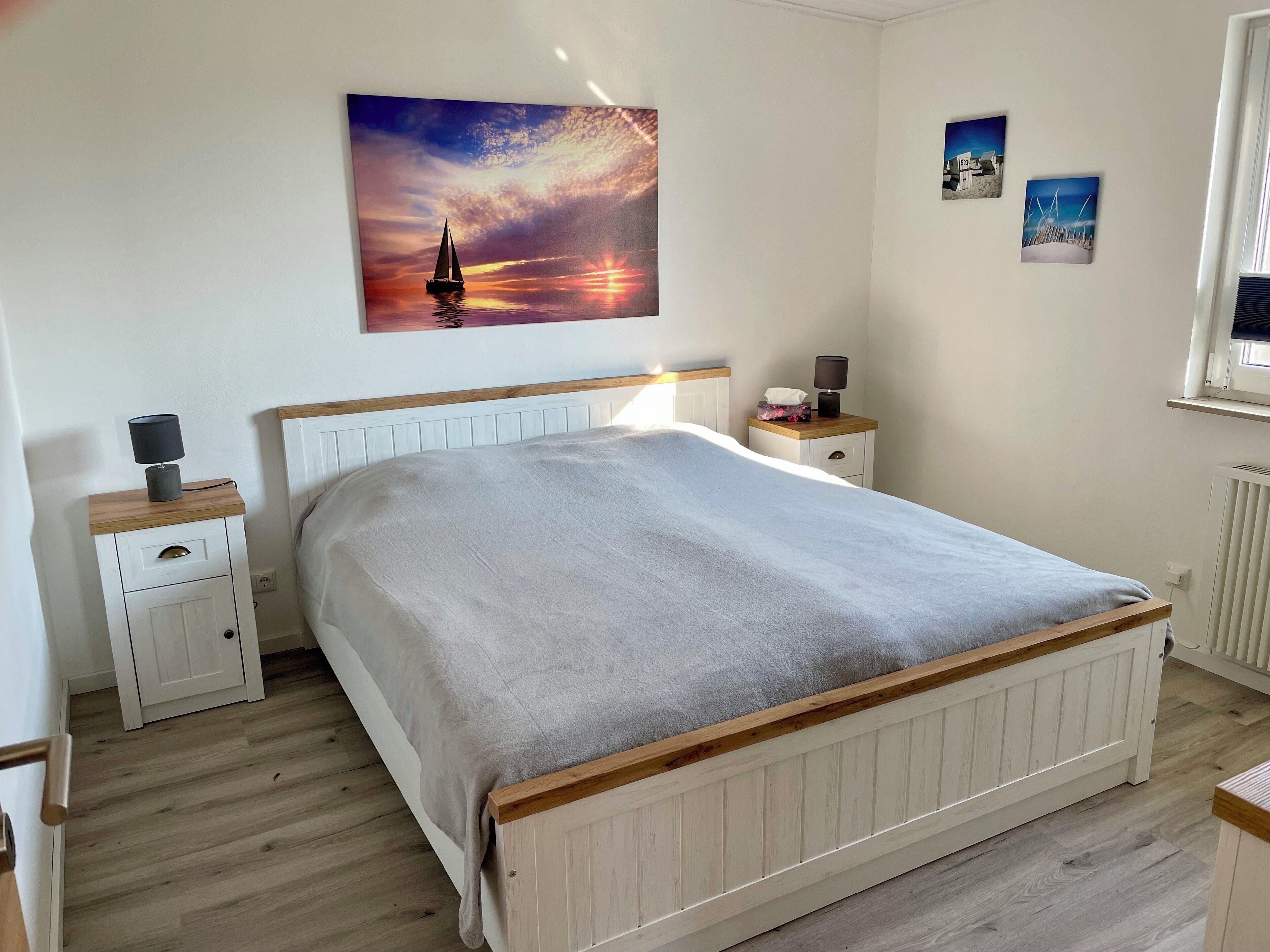 A neatly arranged bedroom with a large bed, wooden headboard, bedside tables with lamps, and a wall-mounted painting.