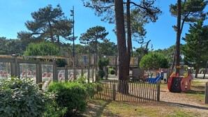 A playground with a wooden fence, trees, and a clear sky. - Mobilhome 6 pers (Vendays-Montalivet)