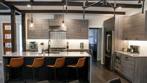 A modern kitchen with a central island, bar stools, pendant lighting, and stainless steel appliances.