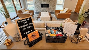 A cozy living room with a stone fireplace, leather sofas, and a welcome sign for Whispering Pines LUXE Lodge 2025.