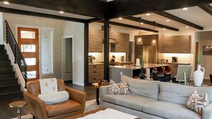 A modern living room with a sofa, armchair, and ottoman. A staircase with a wooden railing leads to another room.