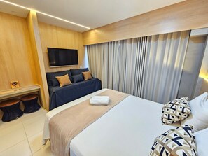 A modern hotel room with a bed, a sofa, a TV, and a wooden accent wall. - Makia - Porto de Galinhas  (Ipojuca)