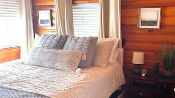 Une chambre aménagée dans une cabane en bois, avec un lit, des rideaux, un climatiseur fixé au mur, une lampe de chevet et une petite plante en pot.