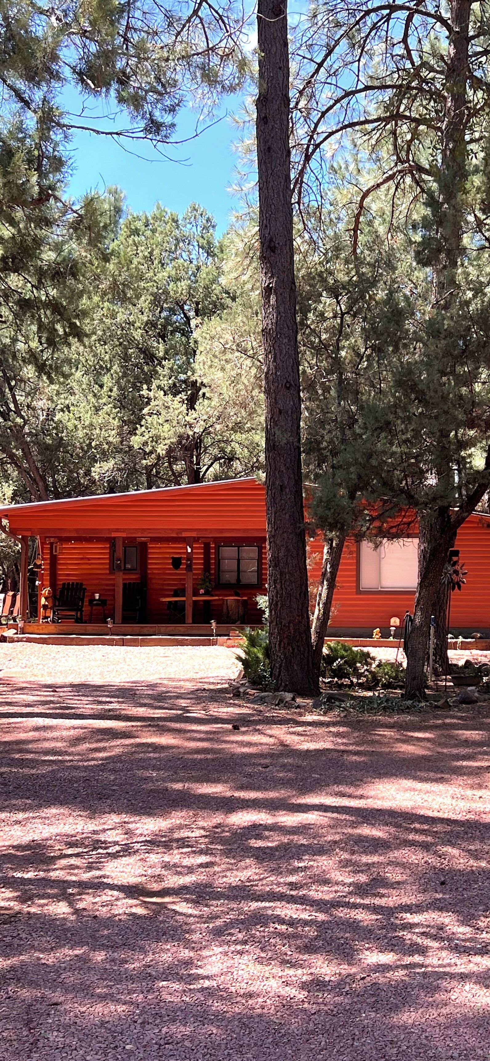 Une cabane rustique à l’extérieur rouge, entourée d’arbres et bordée d’une allée de gravier.