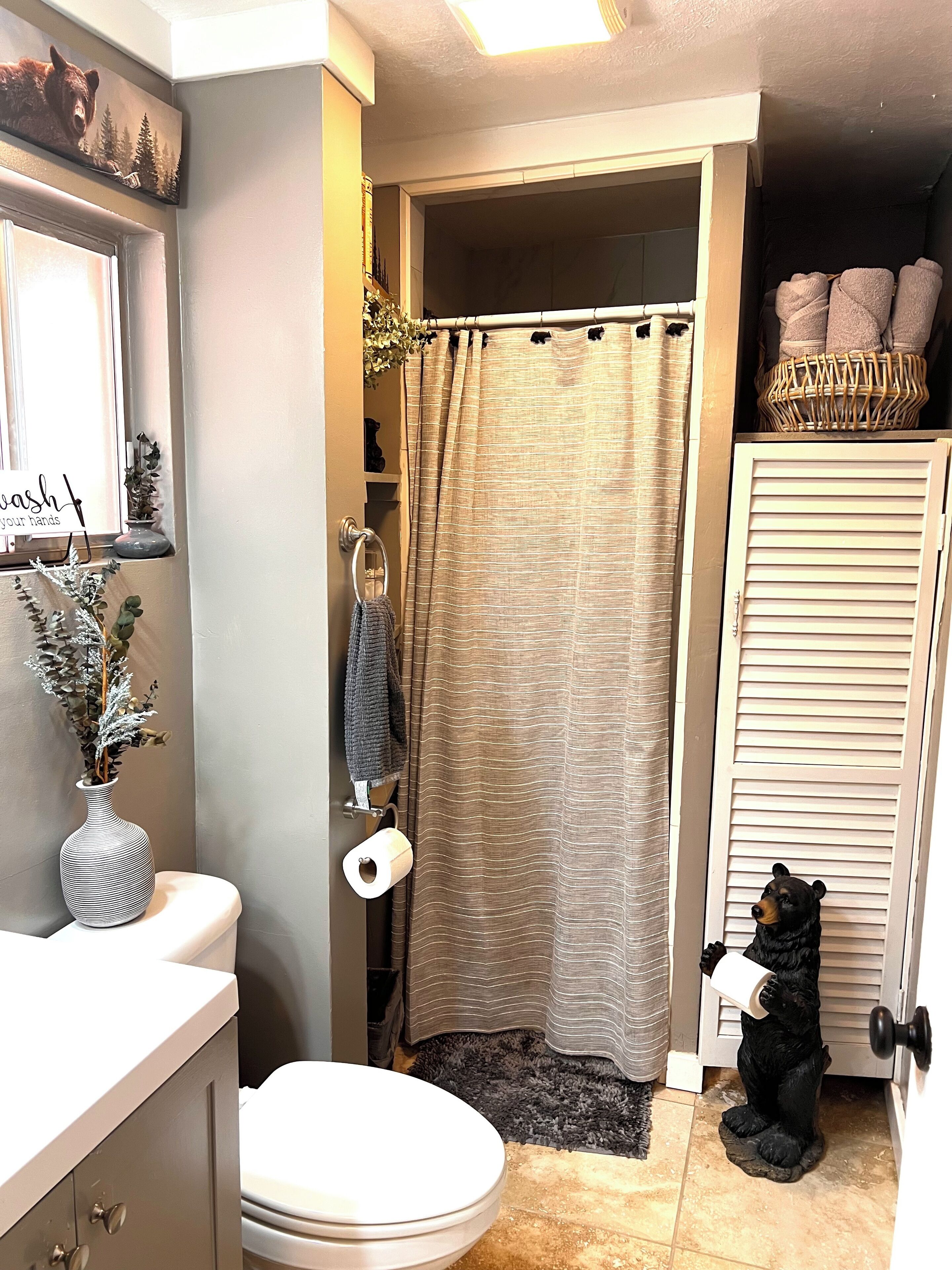 Une salle de bain équipée de toilettes, d’un rideau de douche, d’un porte-serviettes et d’une statue d’ours décorative.