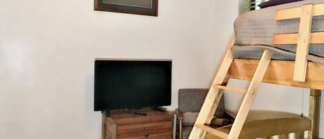 Un dormitorio con una cama litera, un televisor sobre un aparador de madera, un cuadro enmarcado en la pared y una ventana con persianas.