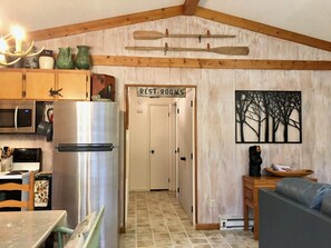 A kitchen with a stainless steel refrigerator, wooden cabinets, and a microwave. There is a sign above a door that reads "RESTROOMS".