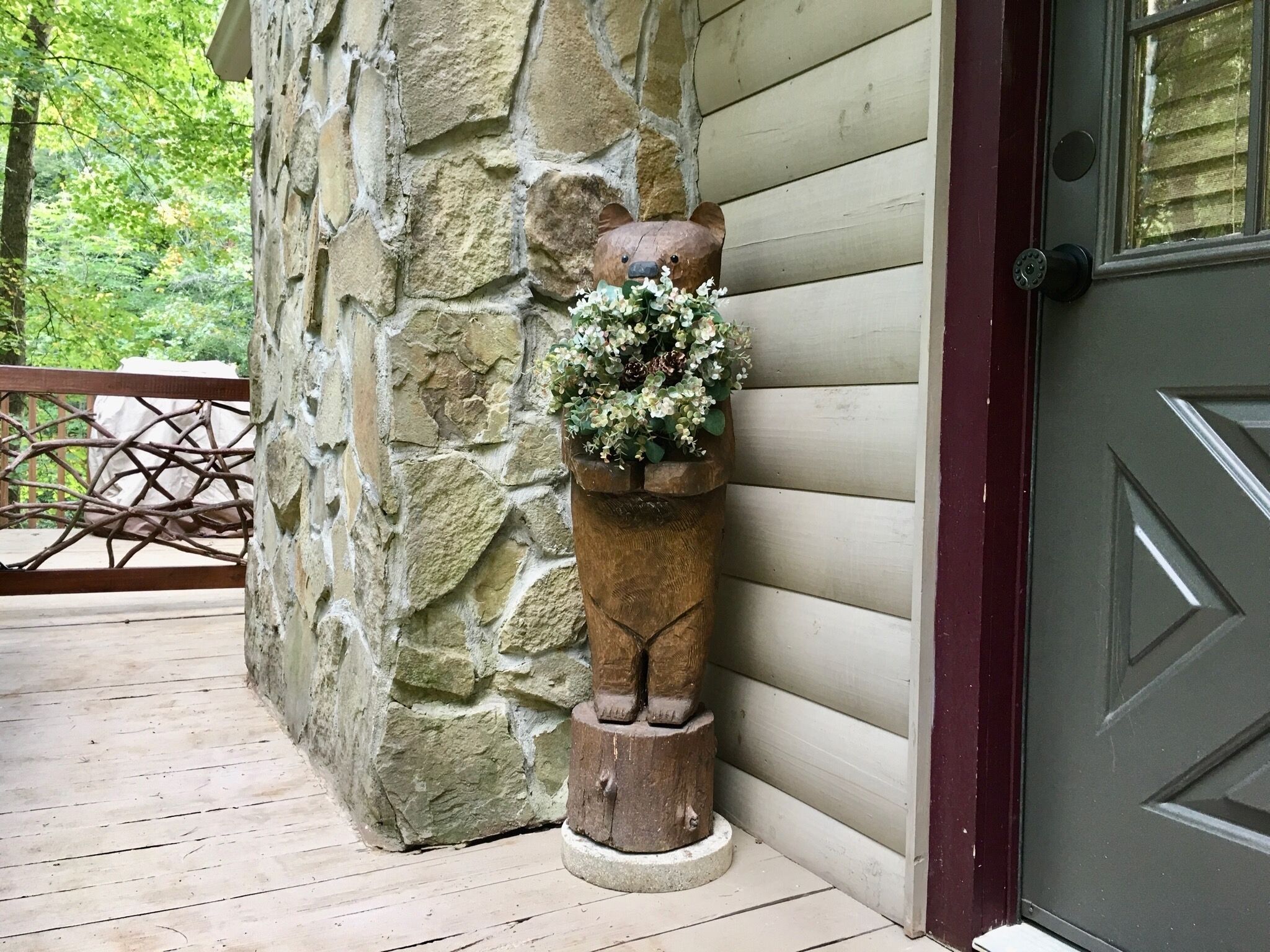 Un mur en pierre surmonté d’un jardinier en bois contenant une petite plante, un banc en bois et une porte ornée d’un motif géométrique.
