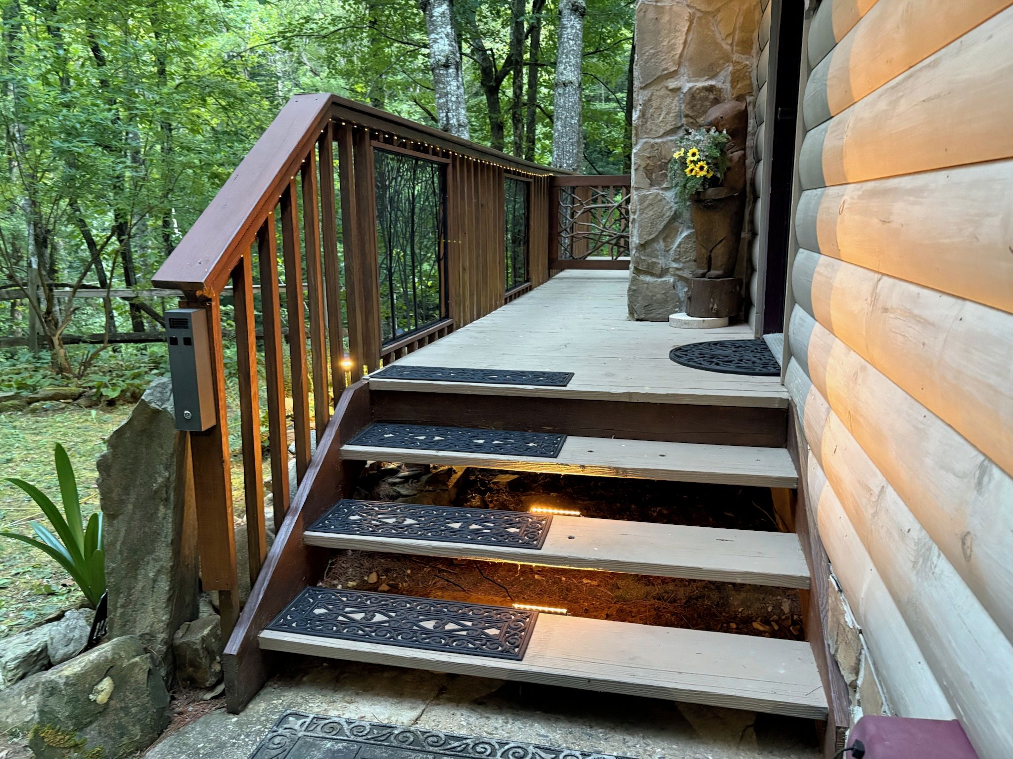 A wooden staircase leading to a log cabin with a stone wall and a flower arrangement.