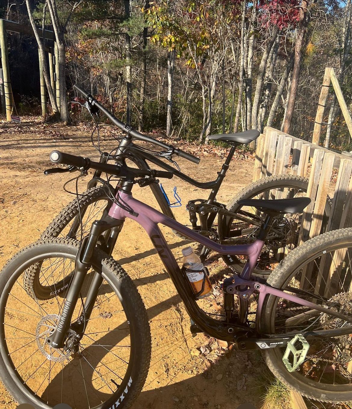 A mountain bike parked on a dirt path with a wooden fence and trees in the background.