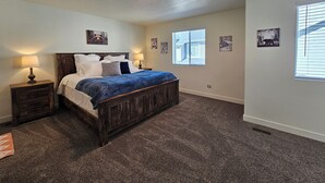Un dormitorio con una cama de madera, dos mesitas de noche con lámparas, suelo cubierto de alfombra y una ventana con persianas.