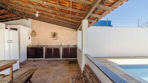 Ein überdachter Außenbereich mit Pool, eine Küche mit Holzschränken und einer hängenden Leuchte.