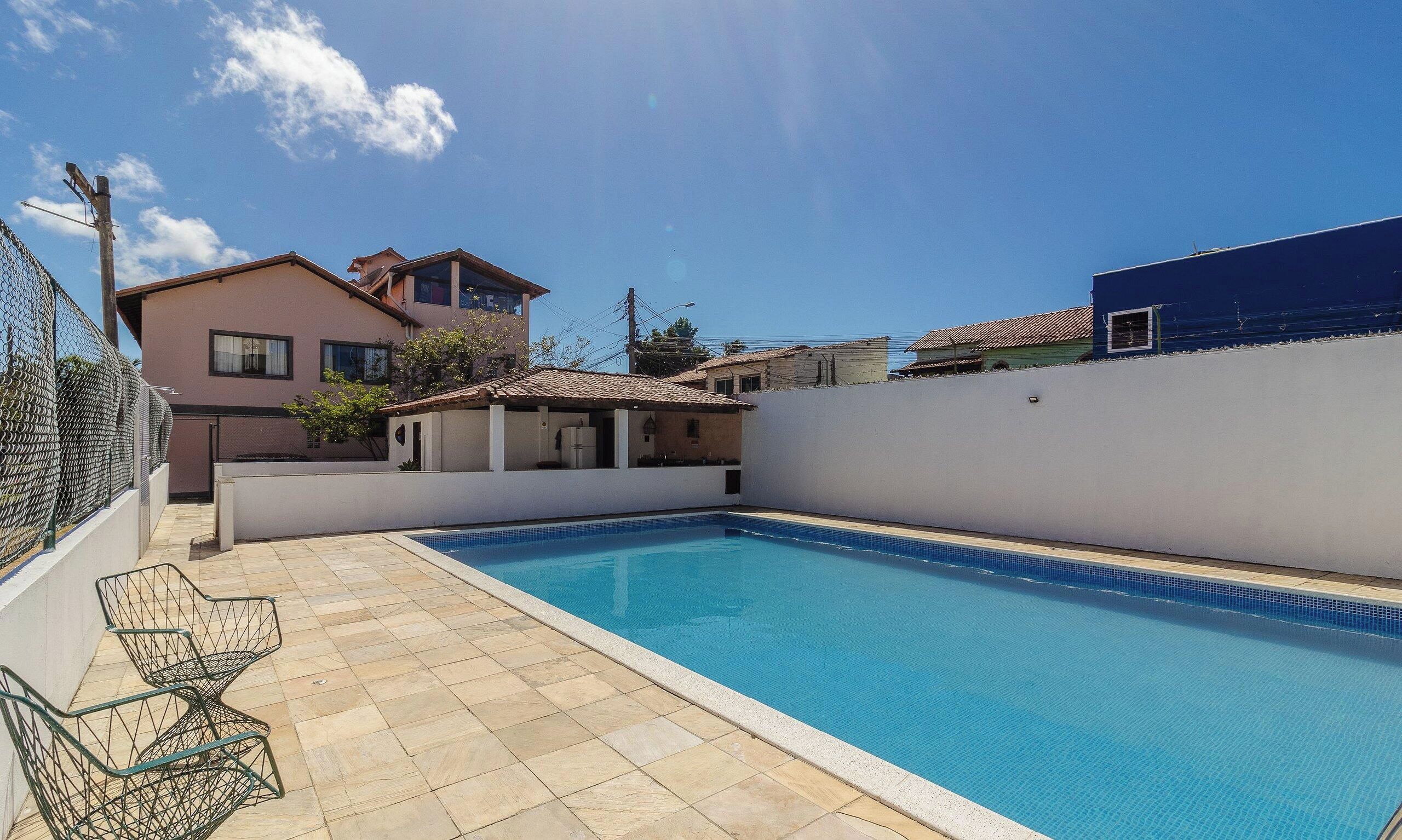 Una piscina con suelo de baldosas, una pequeña construcción contigua y una valla.