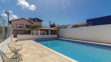 Una piscina con suelo de baldosas, una pequeña construcción contigua y una valla.