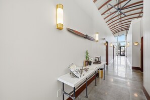 Un couloir avec un comptoir d’accueil blanc, des lampes fixées au mur et un ventilateur de plafond.