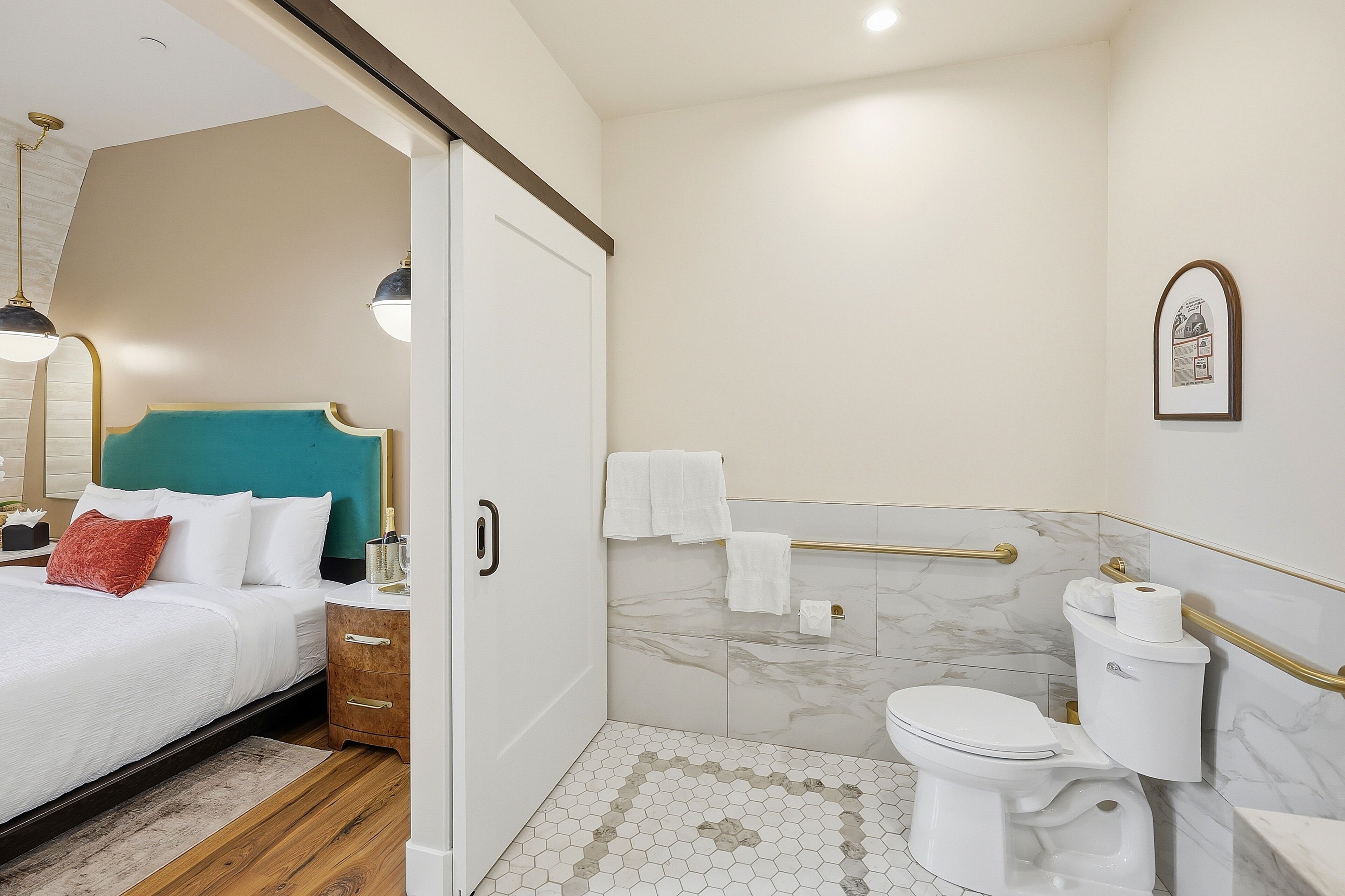 Habitación de hotel con cama, mesita de noche, baño con inodoro, ducha y toallero.