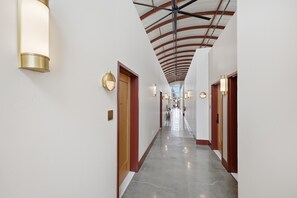A hallway with a polished floor, white walls, and doors with red trim. - The Q Inn (Morro Bay)