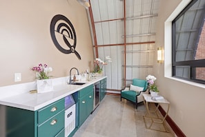 A modern kitchen with a white countertop, teal cabinetry, and a large window. - The Q Inn  (Morro Bay)