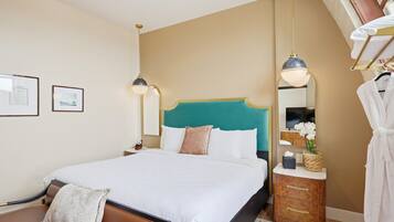 Una cama bien hecha con un cabecero verde aguamarina, una mesita de noche con una lámpara y un espejo con una orquídea en maceta.