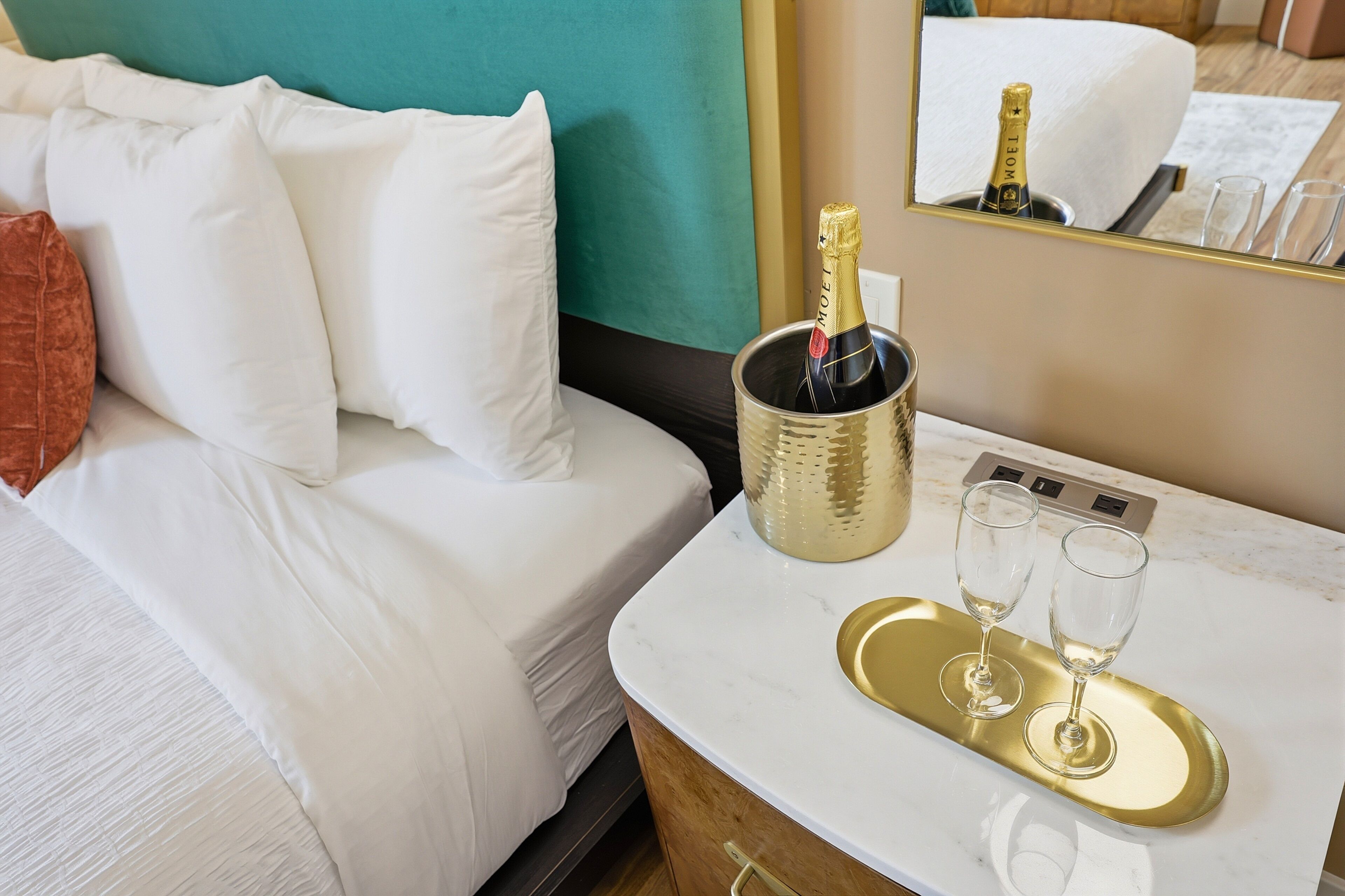 A hotel room with a bed, a minibar, a tray with two glasses, and a bottle of champagne.