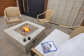 A fire pit with chairs, a table, and a door in the background. - The Q Inn (Morro Bay)