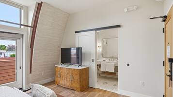 A bedroom with a TV on a wooden cabinet, a sliding door to a bathroom, and a view of the outside.