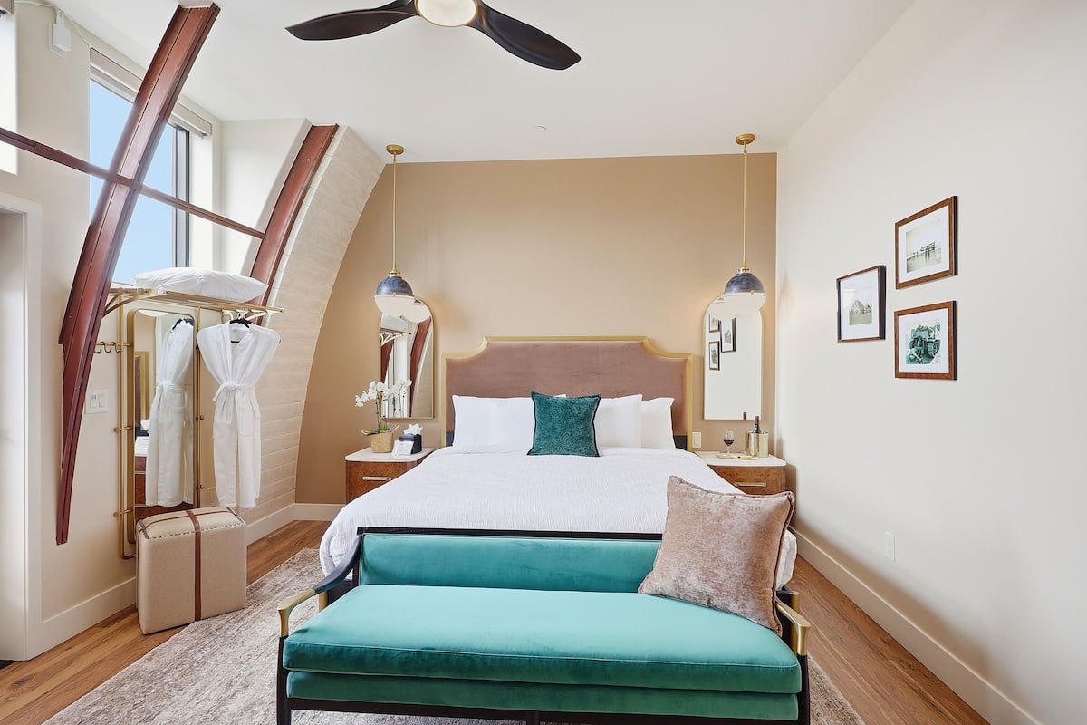 A bedroom with a bed, a bench, a mirror, and framed pictures on the wall.