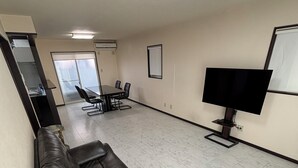 A spacious room with a large leather sofa, a flat-screen TV mounted on the wall, and a conference table with chairs.