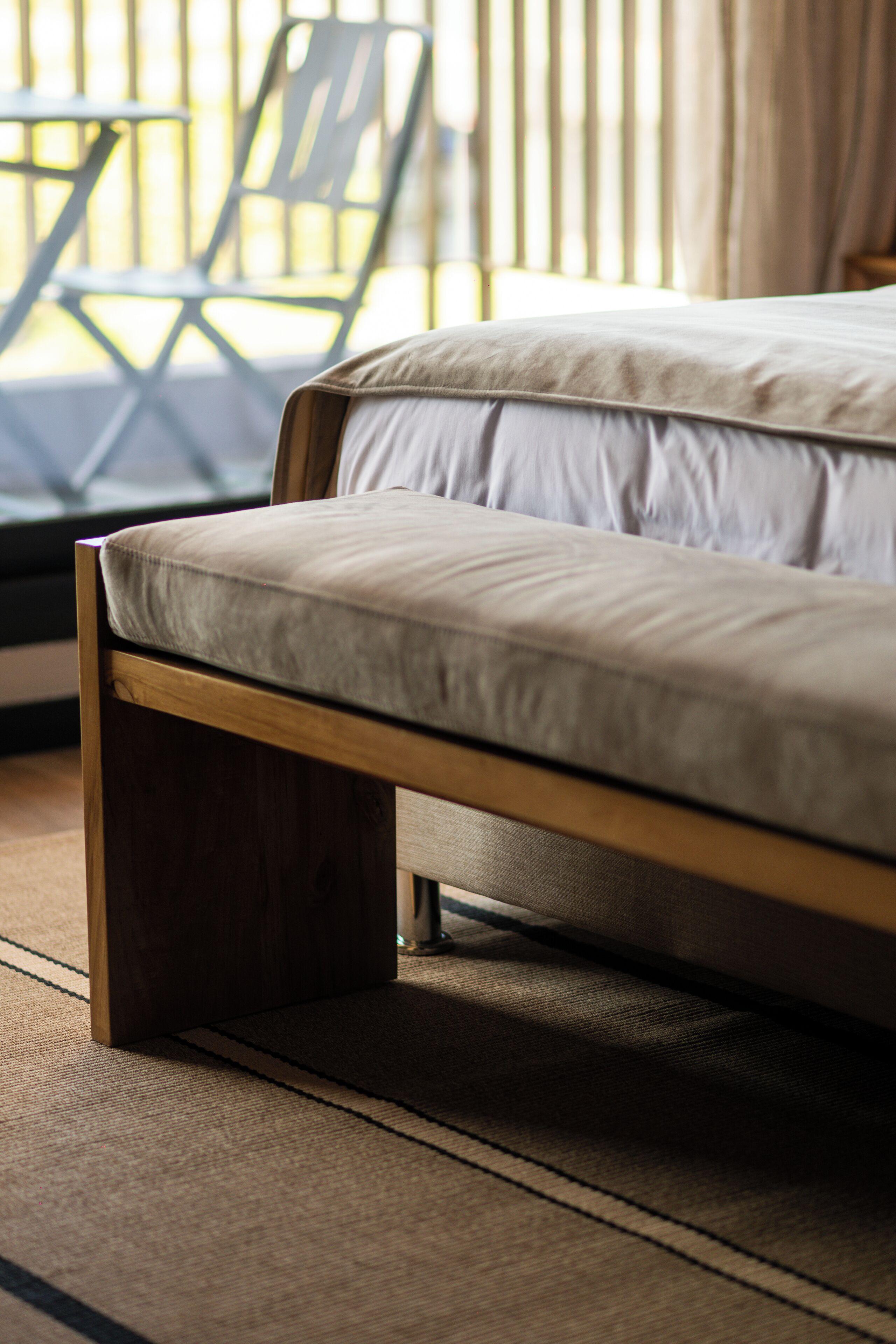 Una cama con estructura de madera y colchón de color claro en una habitación con vistas a muebles de exterior y cortinas.
