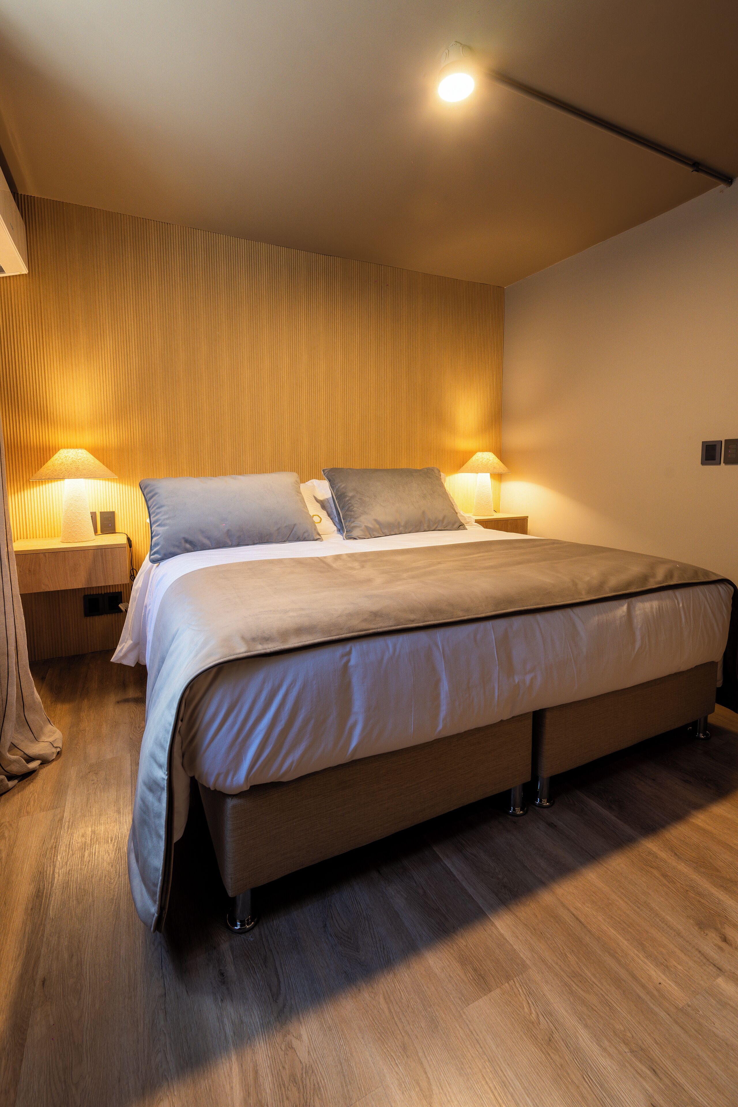 A modern bedroom with a large bed, two bedside tables with lamps, and a wooden wall panel.