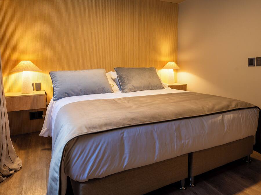 A modern bedroom with a large bed, two bedside tables with lamps, and a wooden wall panel.
