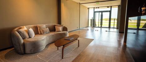 A modern living room with a curved sofa, a wooden coffee table, and a large window offering a view of the outdoors.