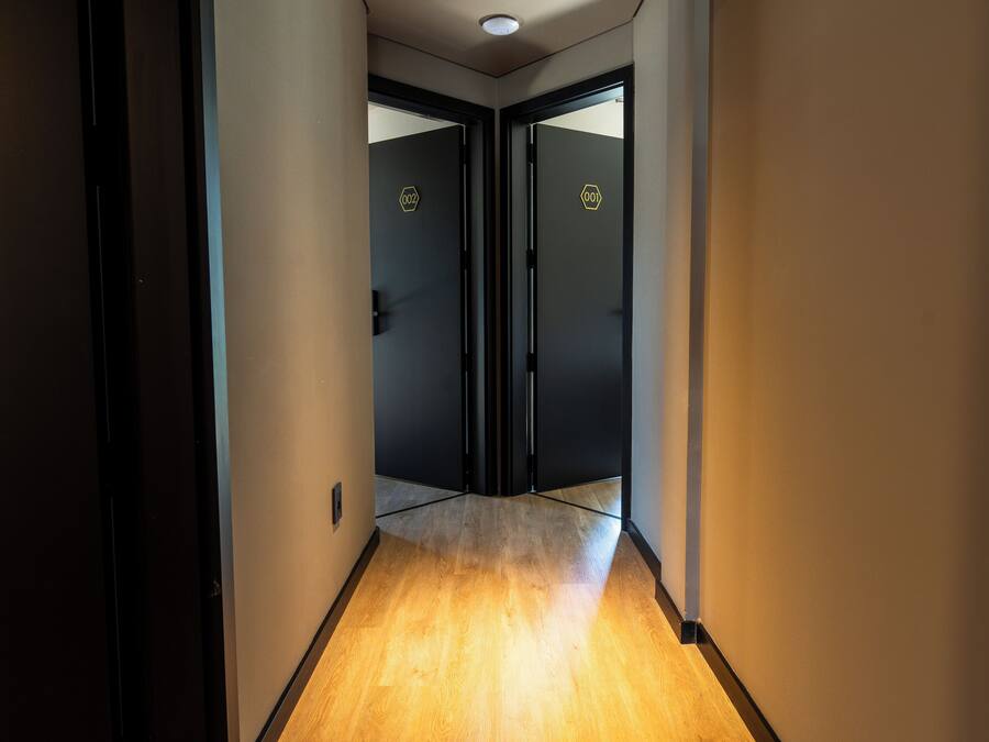 Un pasillo con suelo de madera, puertas negras e iluminación empotrada.