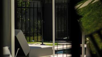 Un espacio exterior moderno para sentarse, con una estructura blanca, cercado por una valla metálica y con follaje al fondo.