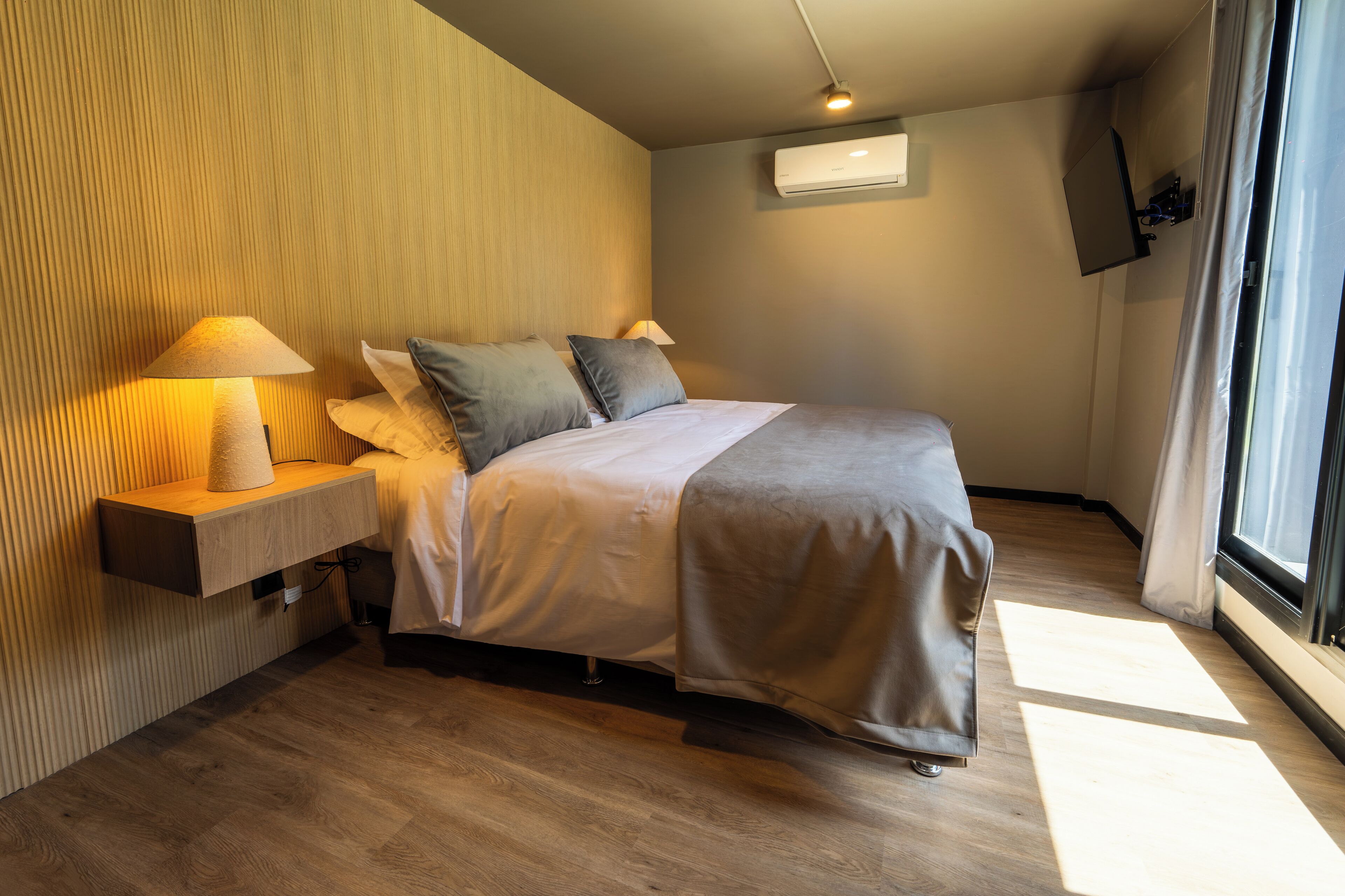 Un dormitorio moderno con cama, lámparas de noche, una mesita de noche de madera y una ventana con cortinas.
