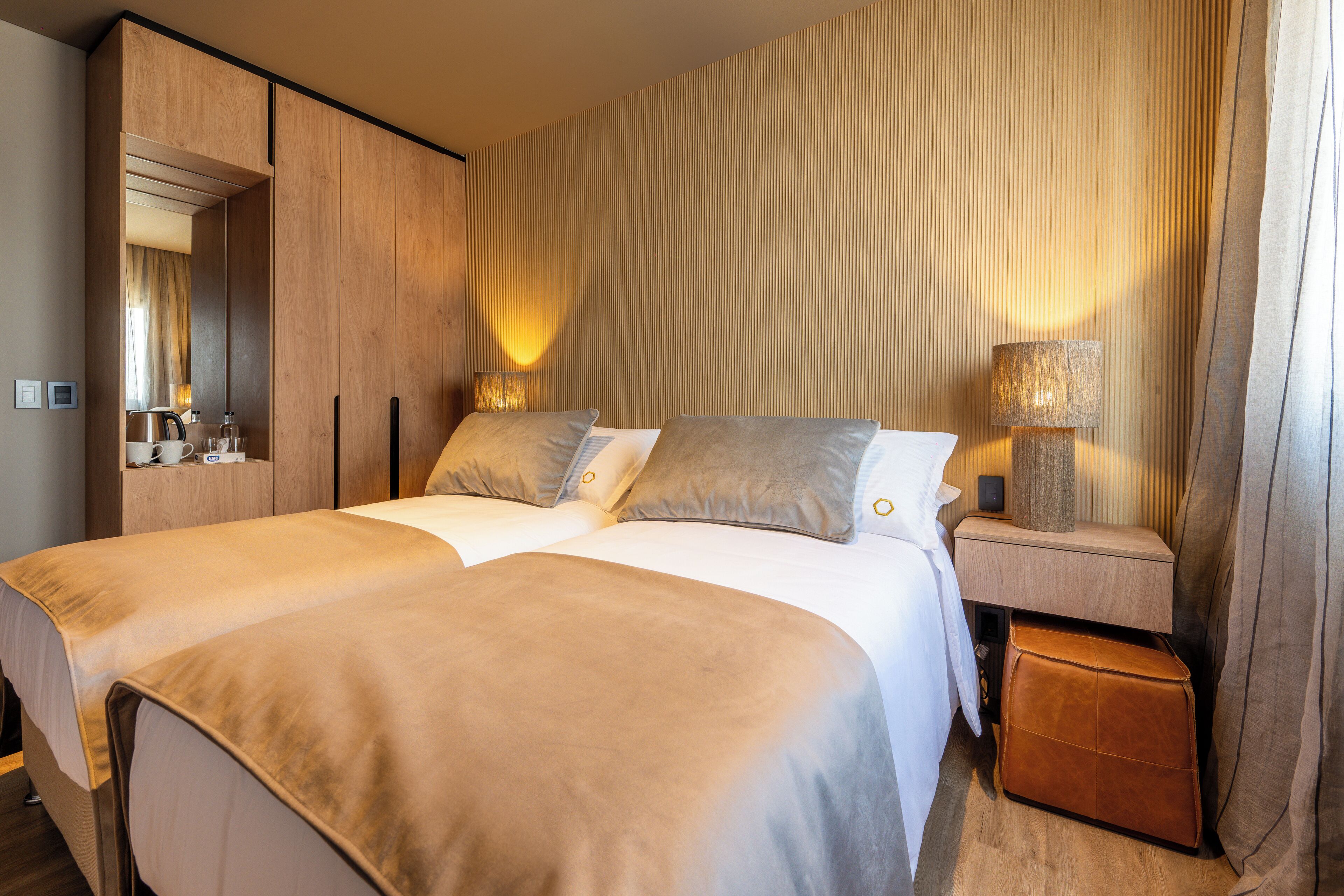 Una cama doble con cabecera de madera, una mesita de noche con lámpara y un pequeño banco de madera.