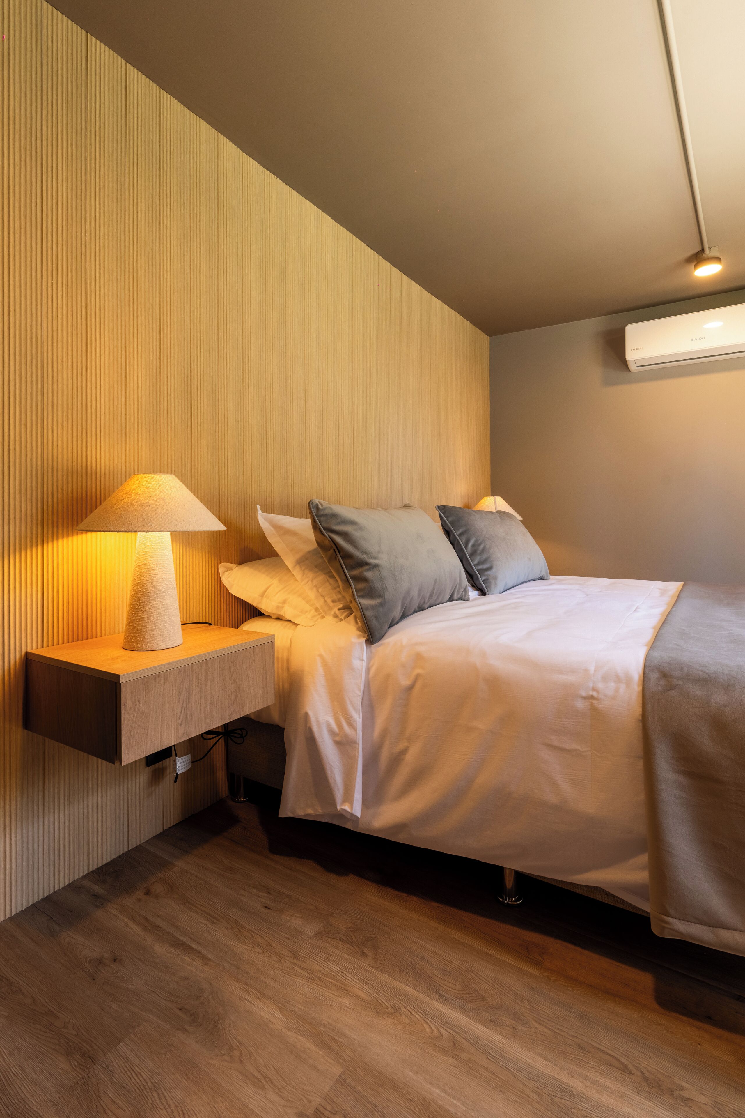A modern bedroom with a bed, bedside table, lamp, and air conditioning unit.
