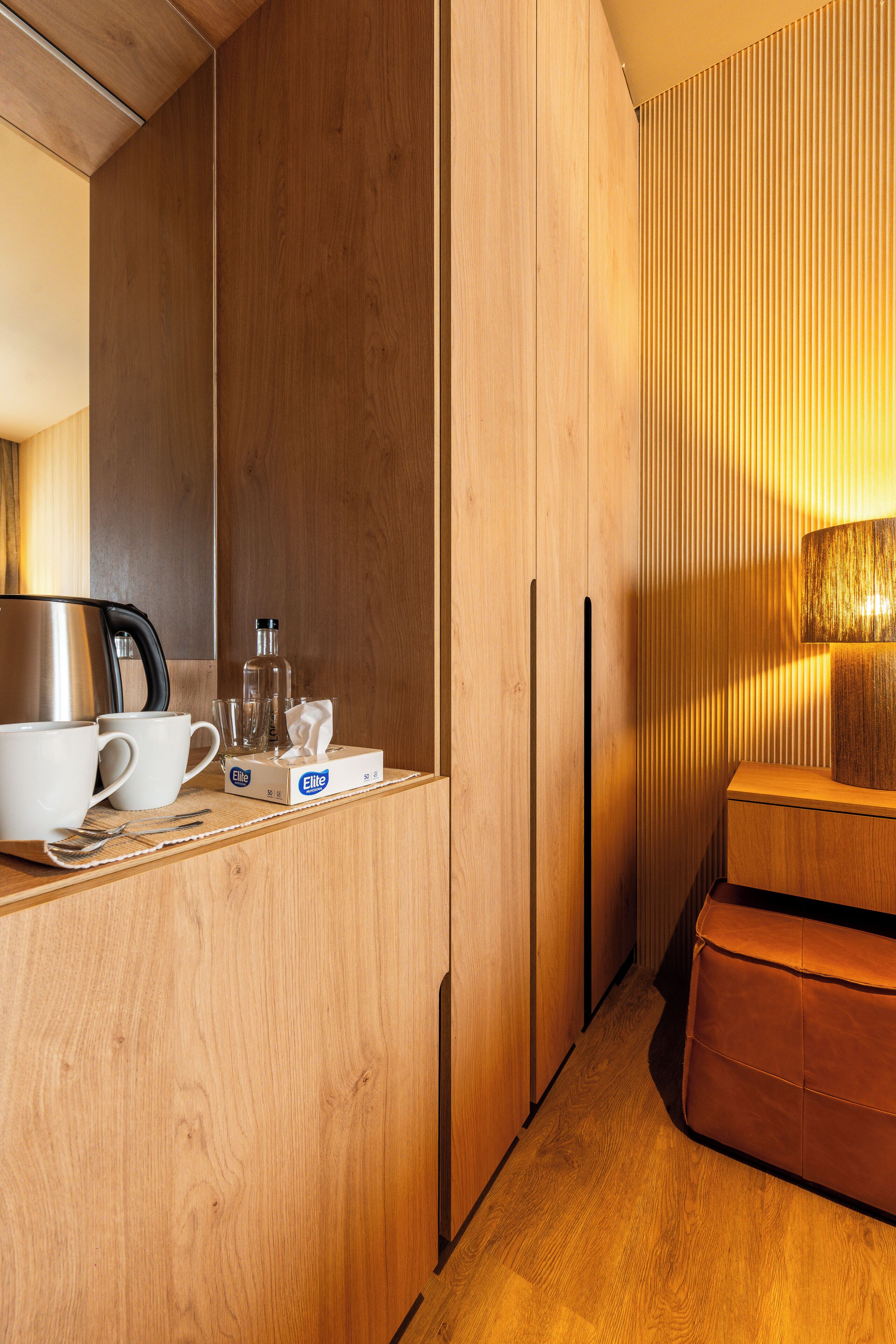 Una kitchenette compacta y moderna con muebles de madera, una cafetera, tazas y una caja de pañuelos.