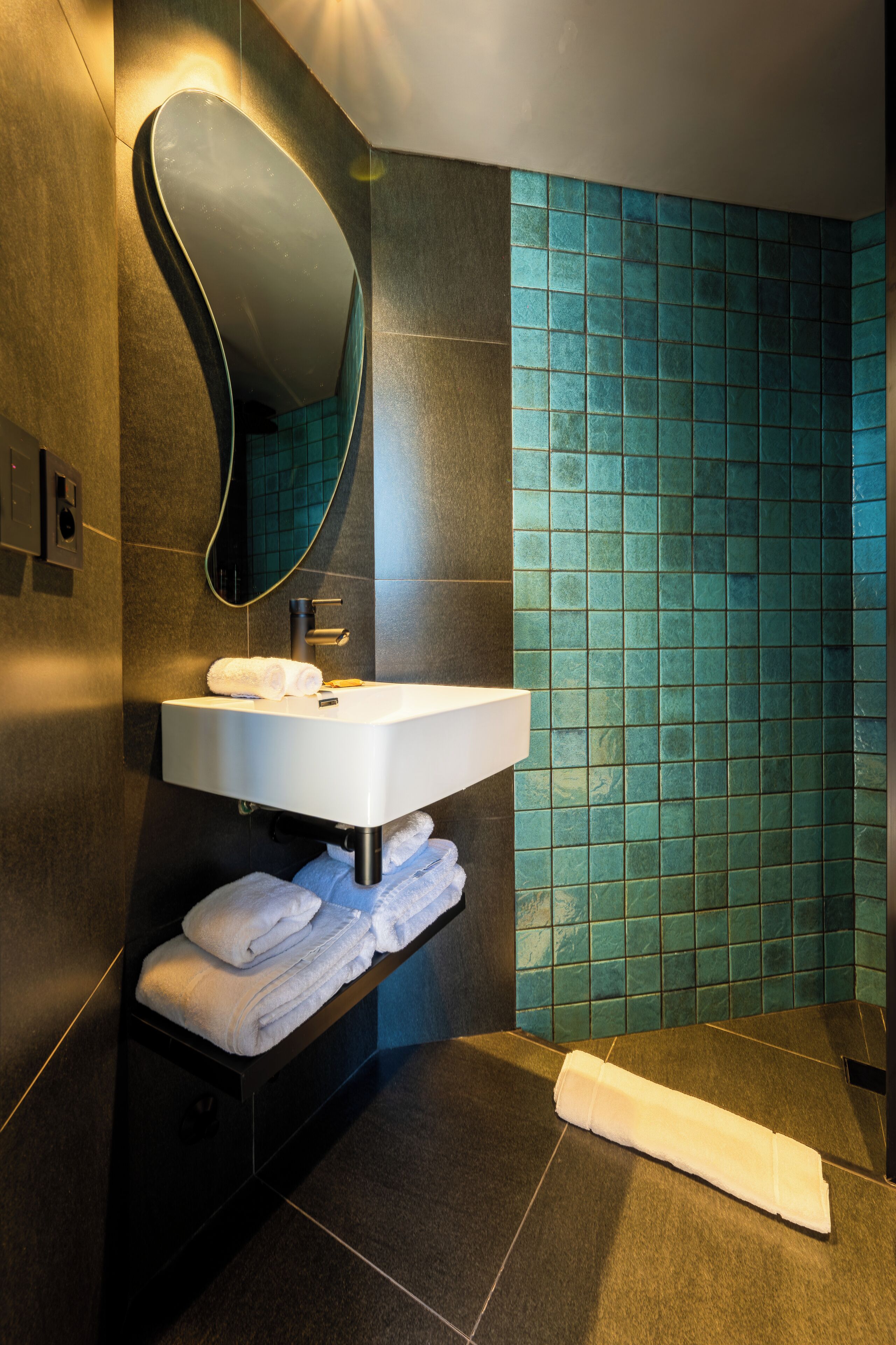 A modern bathroom with a white sink, dark tiles, and a large mirror.