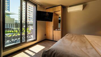 A modern hotel room with a large sliding glass door to the outside, a flat-screen TV mounted on the wall, and a bed with a wooden headboard.