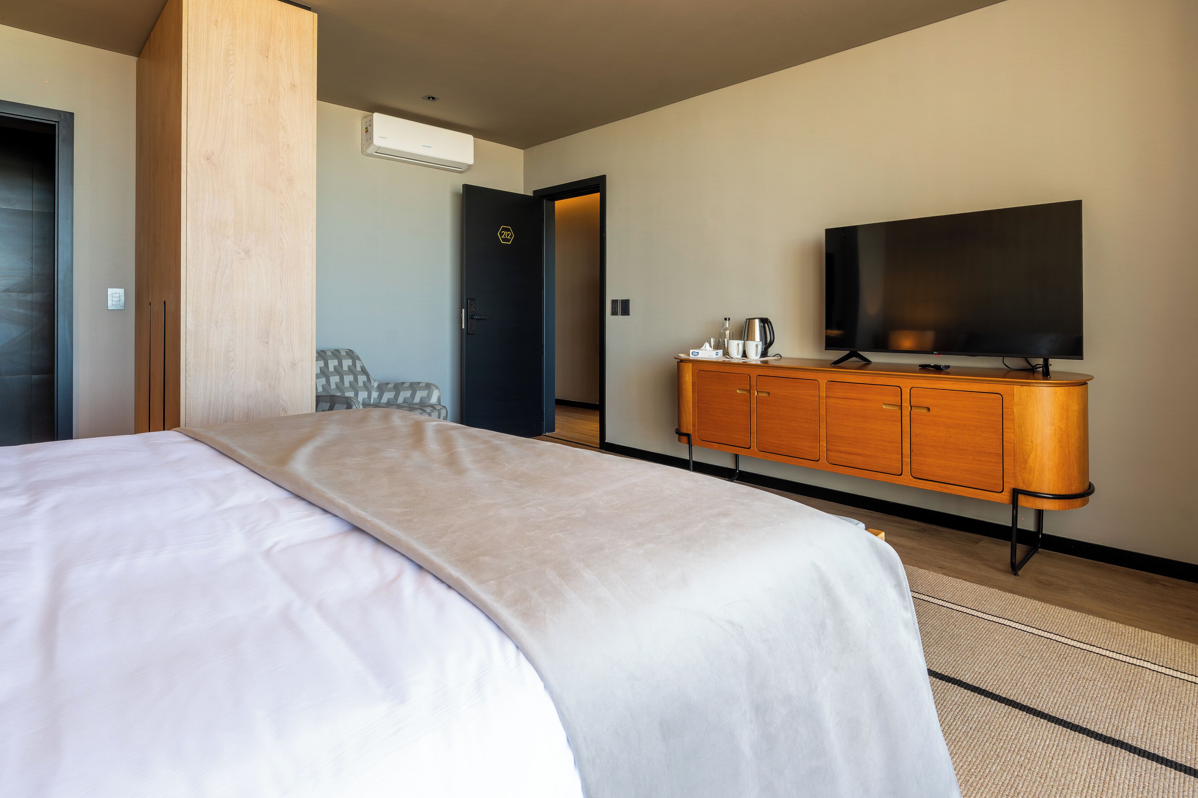 Una habitación de hotel con una cama, un televisor, un armario de madera y una puerta que da a otra habitación.
