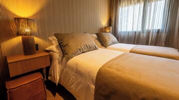 A hotel room with two beds, a wooden nightstand, a lamp, and a window with curtains.