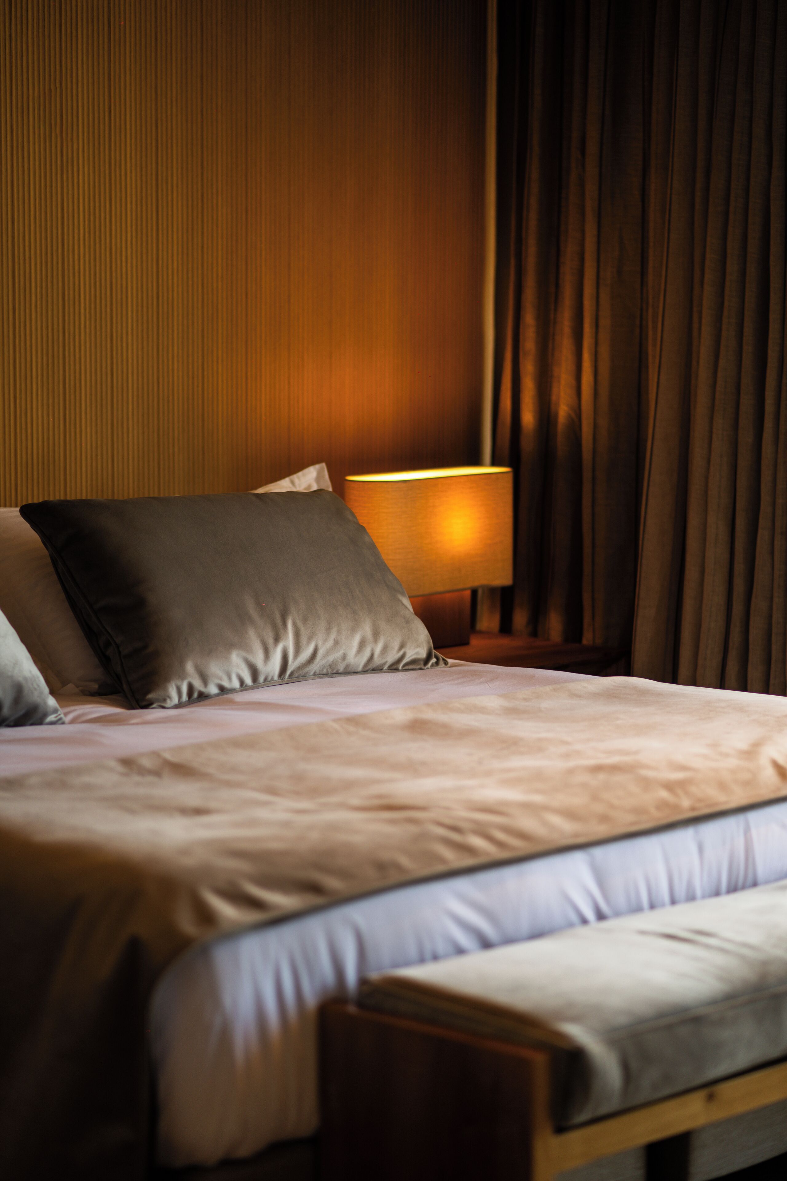 A neatly made bed with pillows, a bedside lamp, and a wooden headboard in a hotel room.