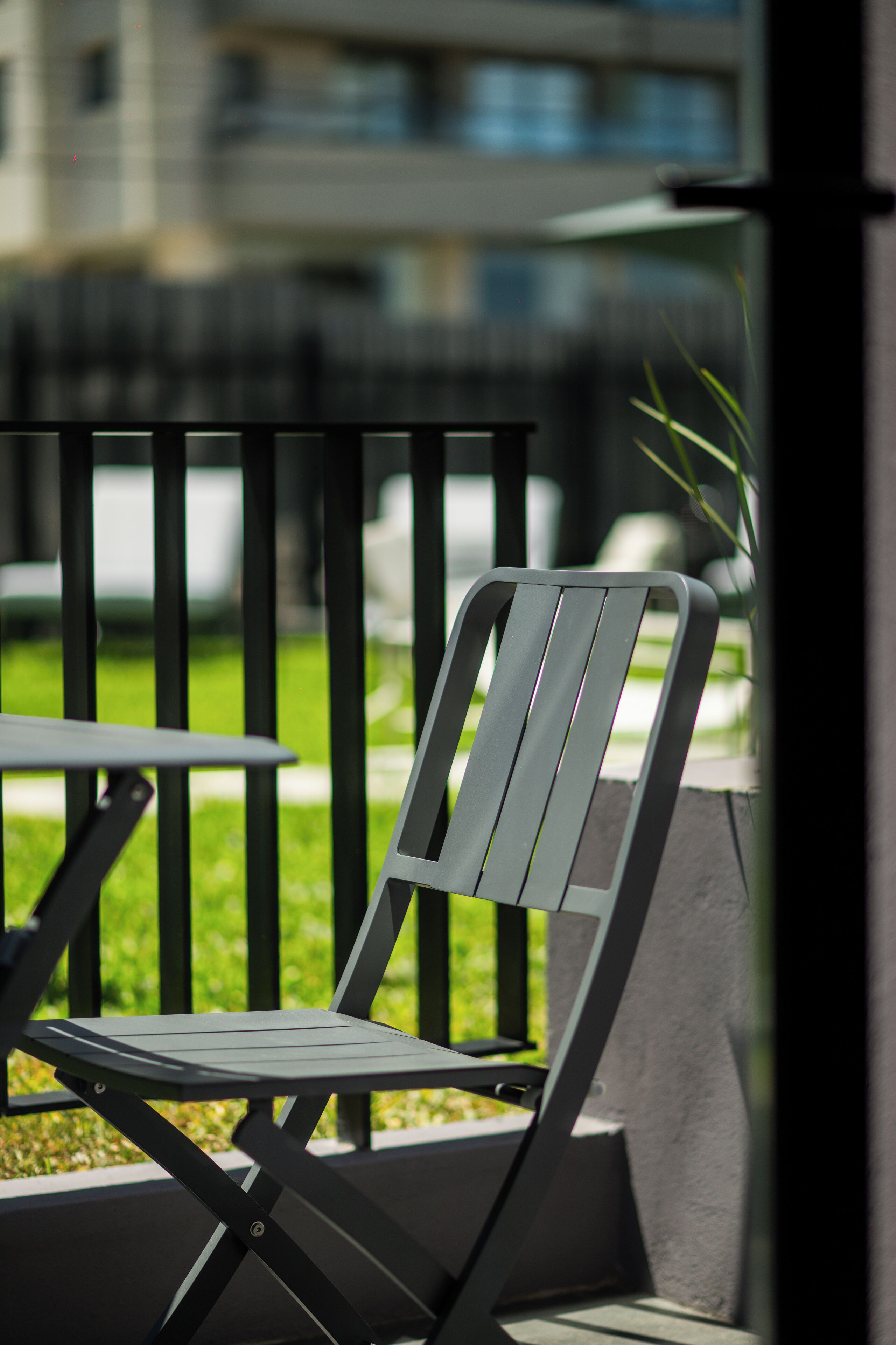 A modern outdoor seating area with a metal chair and table, surrounded by a concrete wall and a metal fence.